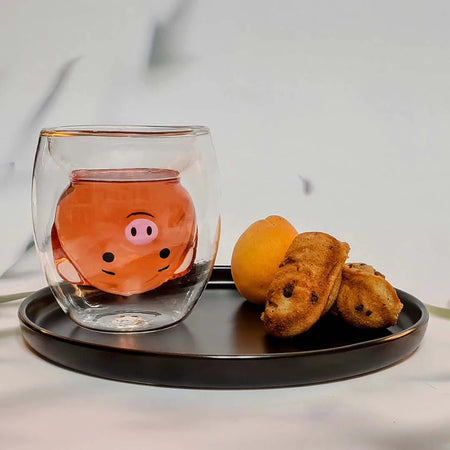 tasse en verre double paroi en forme de cochon sur plateau avec madeleines